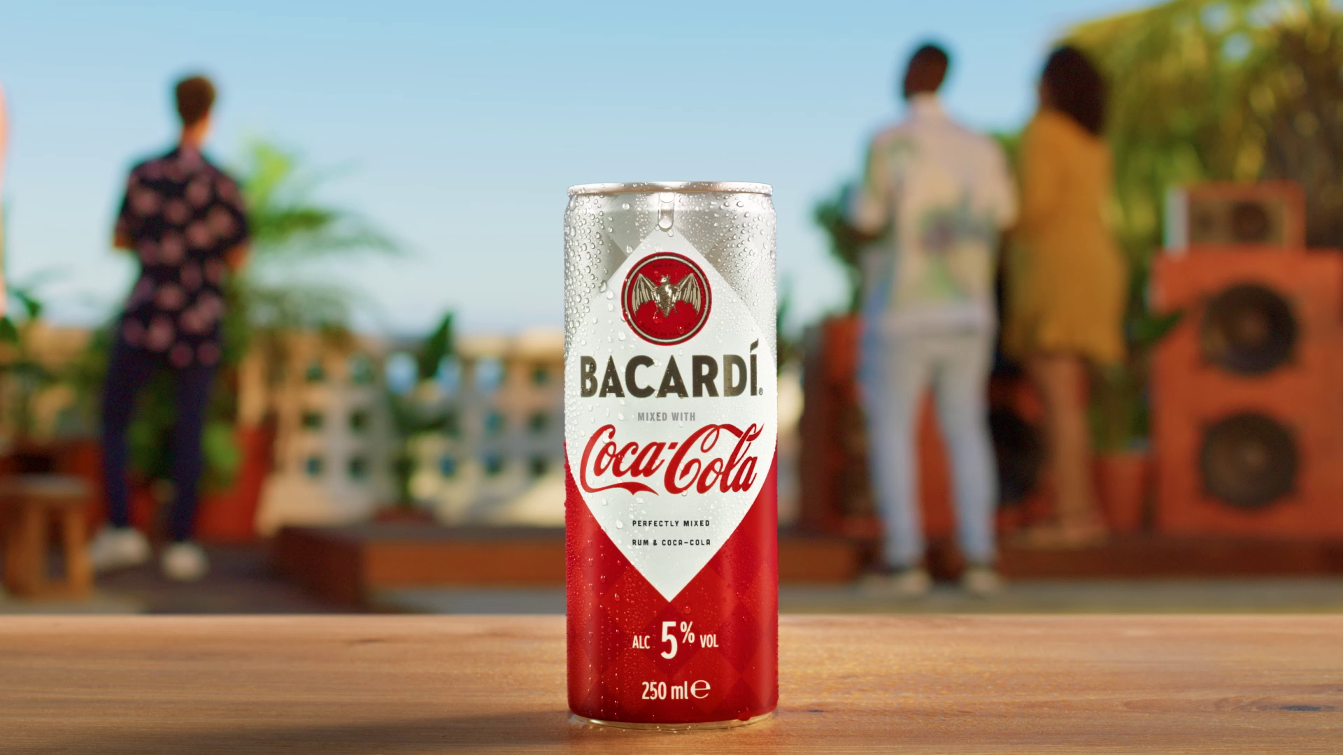 Plechovka Bacardi s Coca-Colou na stole, v pozadí letní terasa.